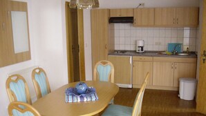 Een compacte keuken met houten kastjes, een eettafel met stoelen en een klein aanrecht met een koffiezetapparaat.