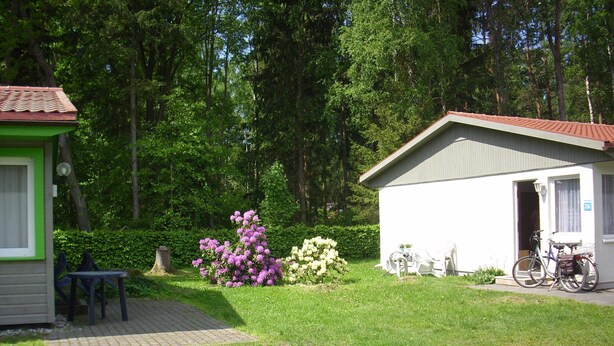 Een laag, enkelvoudig gebouw met een pannendak, omringd door een goed onderhouden tuin met diverse bloeiende planten.