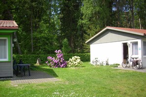 A small, single-story building with a tiled roof, surrounded by a well-maintained garden with various flowering plants. - Ferienwohnung 26, Deutschland (Trassenheide)