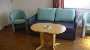 Een kamer met een blauwe bank, een gestreepte fauteuil en een houten tafel met een glazen object erop.