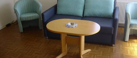 Ein Zimmer mit einem blauen Sofa, einem gestreiften Sessel und einem Holztisch mit einem Glasobjekt darauf.