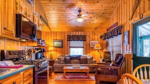 A cozy cabin interior with wooden walls, a kitchenette, a living area with a sofa and coffee table, and a dining table. - Niboban Cabin 5 right on Rangeley Lake with a screened porch, fire pit, hammock, WiFi and dock! (Rangeley)