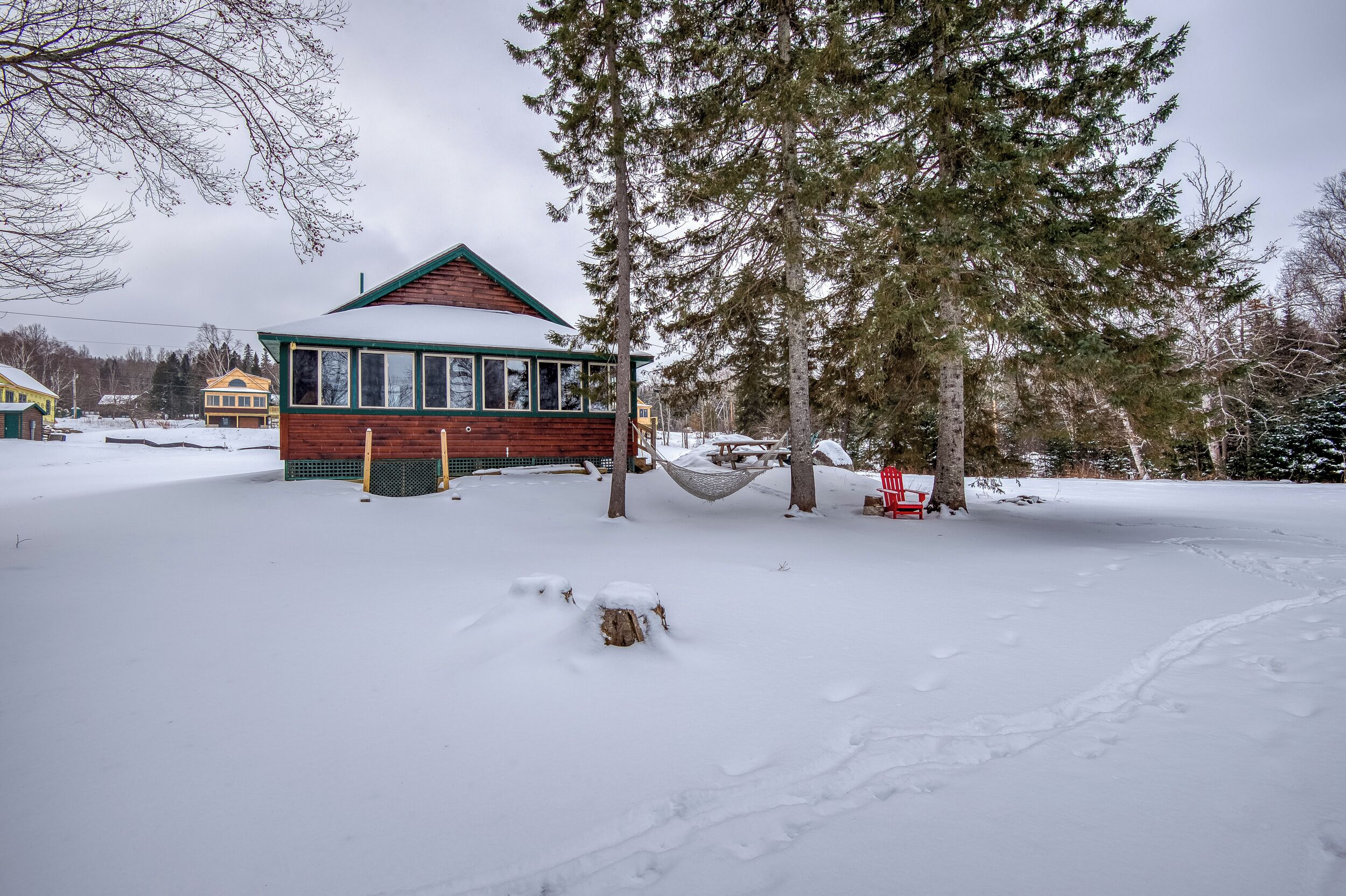 Une cabane en bois avec un toit vert, entourée d’un paysage enneigé et d’arbres.