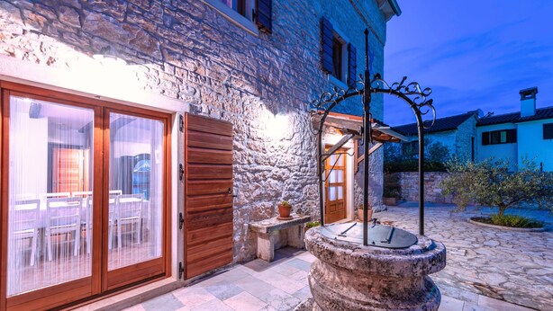 A stone building with a wooden door, a courtyard with a stone fountain, and a view of the sea. - Renoviertes Istrisches Haus (Peresiji)