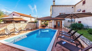 A swimming pool with lounge chairs and umbrellas, surrounded by stone walls and a building with a tiled roof. - Renoviertes Istrisches Haus (Peresiji)