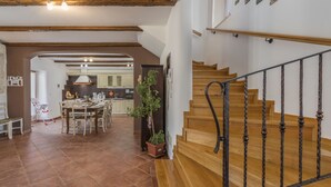 A spacious dining area with a wooden table and chairs, a kitchen in the background, and a wooden staircase with a metal railing. - Renoviertes Istrisches Haus (Peresiji)
