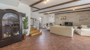 A spacious living room with a wooden staircase, a large cabinet with glass doors, and a stone wall. - Renoviertes Istrisches Haus (Peresiji)