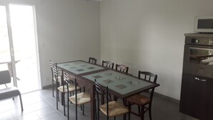 Un espace repas avec une table rectangulaire entourée de chaises, un coin cuisine équipé d’un four à micro-ondes et d’un four traditionnel, et une porte donnant sur un espace extérieur.