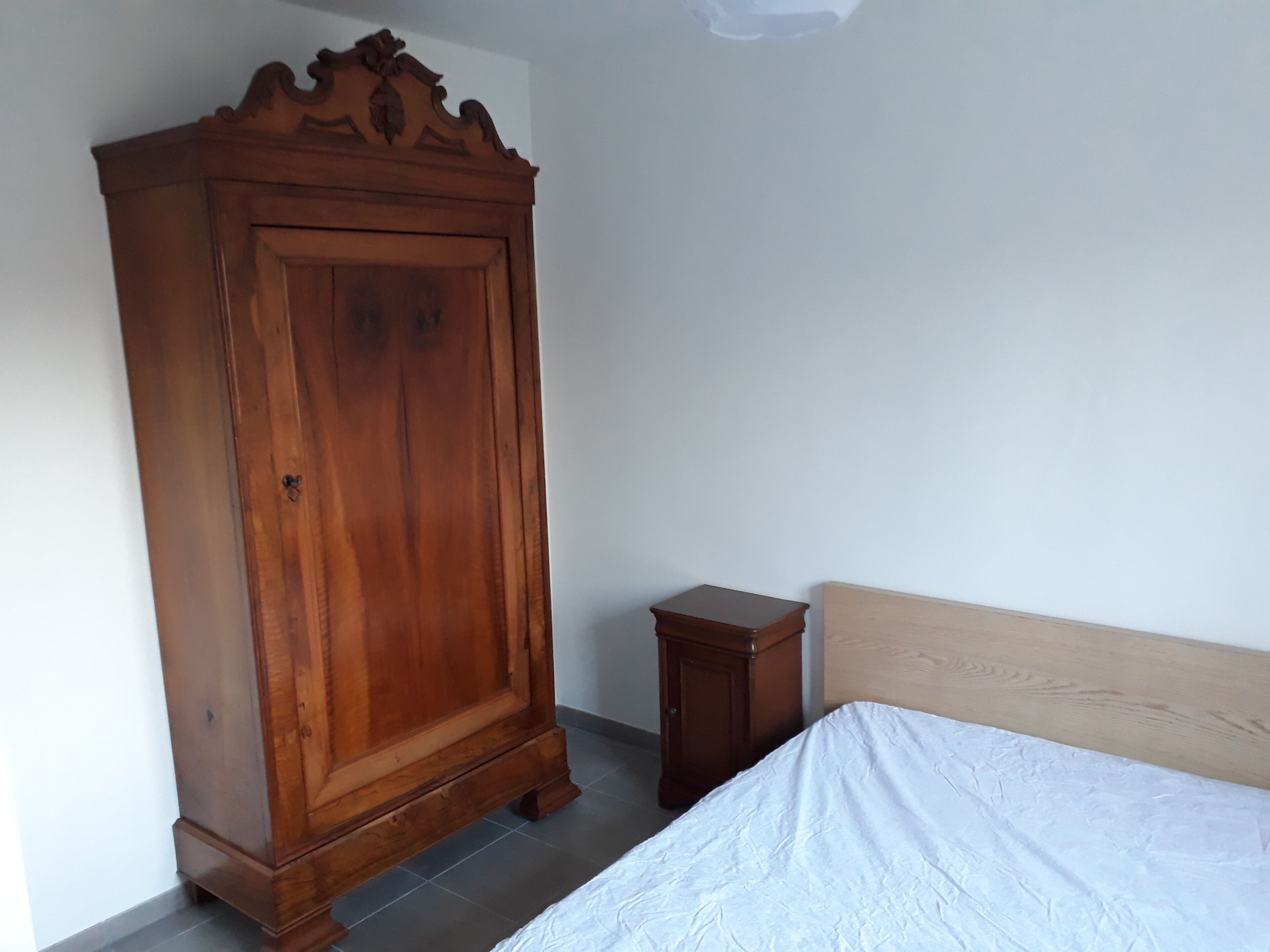 Une chambre avec une armoire en bois, une petite table de chevet et un lit doté d’une tête de lit en bois.