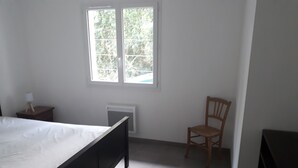 Une chambre à coucher comprenant un lit, une chaise, une table de chevet, une fenêtre et un radiateur.