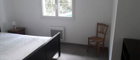 Ein Schlafzimmer mit Bett, Stuhl, Nachttisch, Fenster und Heizkörper.