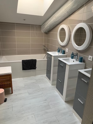 Een moderne badkamer met een badkuip, twee wasbakken en een wastafelmeubel.