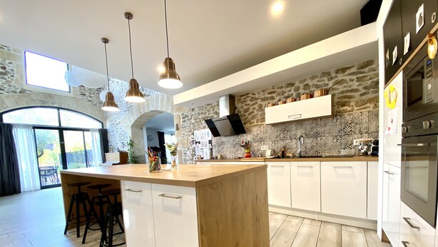 A modern kitchen with a central island, white cabinetry, and a stone accent wall.