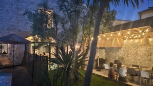 An outdoor dining area with stone walls, tables, chairs, and string lights.