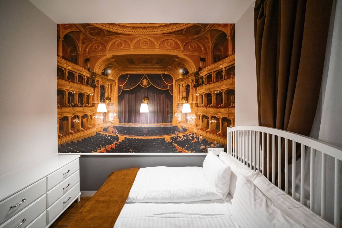 Una habitación de hotel con una cama grande, un tocador blanco y un mural de un teatro ricamente decorado.