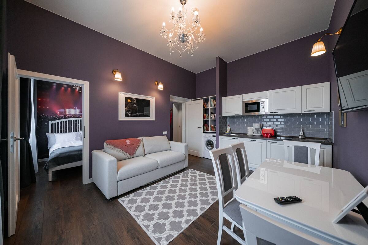 Una sala de estar moderna con un sofá, una mesa de comedor y una cocina con armarios blancos y un microondas.
