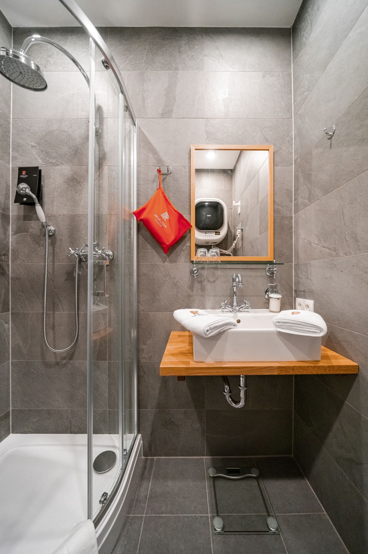 Un baño moderno con ducha envuelta en vidrio, tocador de madera y espejo sobre el lavamanos.
