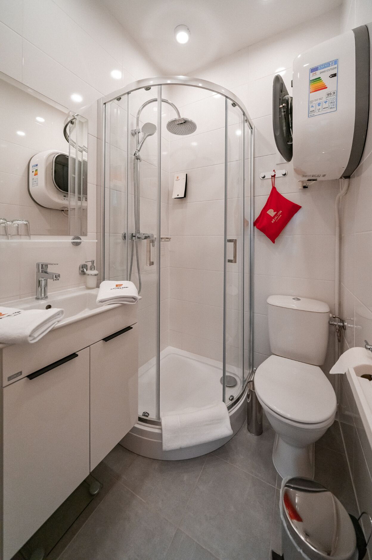 Ein modernes Badezimmer mit einer Duschkabine, einer Toilette und einem Waschbecken mit Handtuchspender.