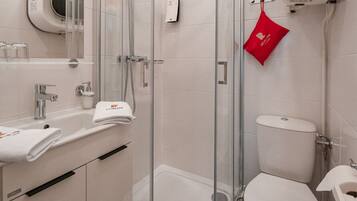 A modern bathroom with a glass-enclosed shower, a toilet, and a sink with a towel dispenser.