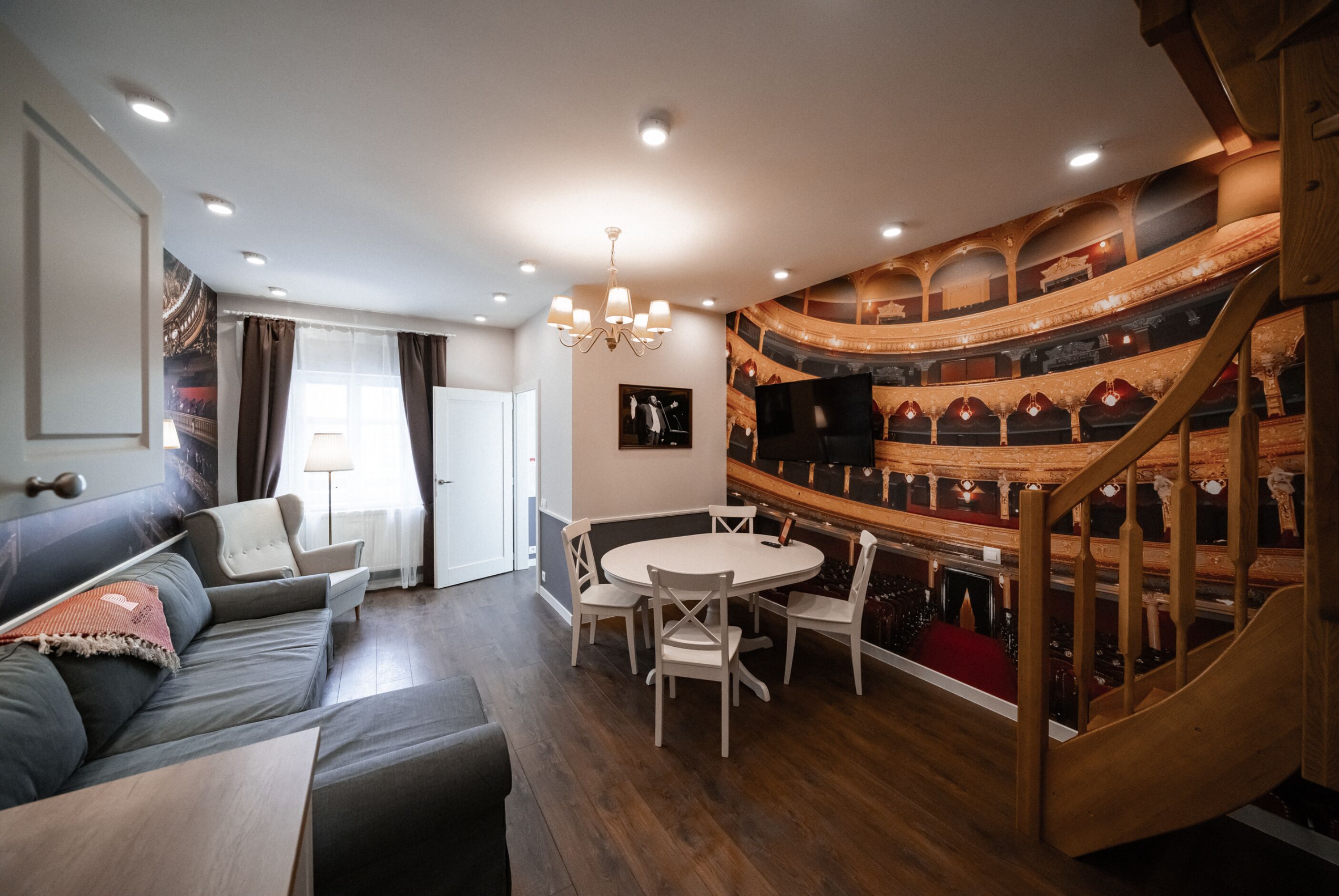 En moderne stue med sofa, spisebord og stole. En trappe med trægelænder fører op til en etage.