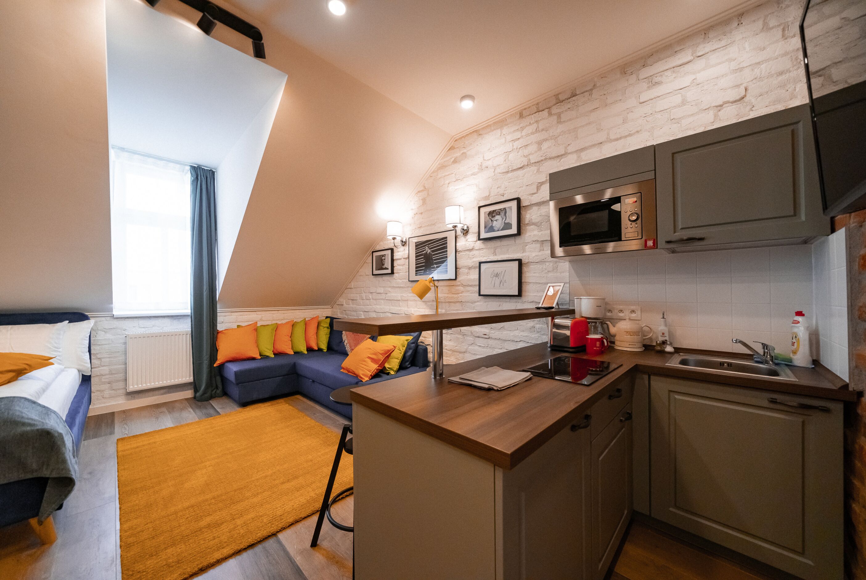 Una cocina moderna con microondas integrado, cafetera y pileta. Cuenta con una encimera de madera y una ventana con cortinas.