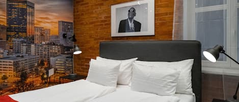A hotel room with a cityscape mural, a bed with white linens, a black headboard, and a framed picture on the wall.