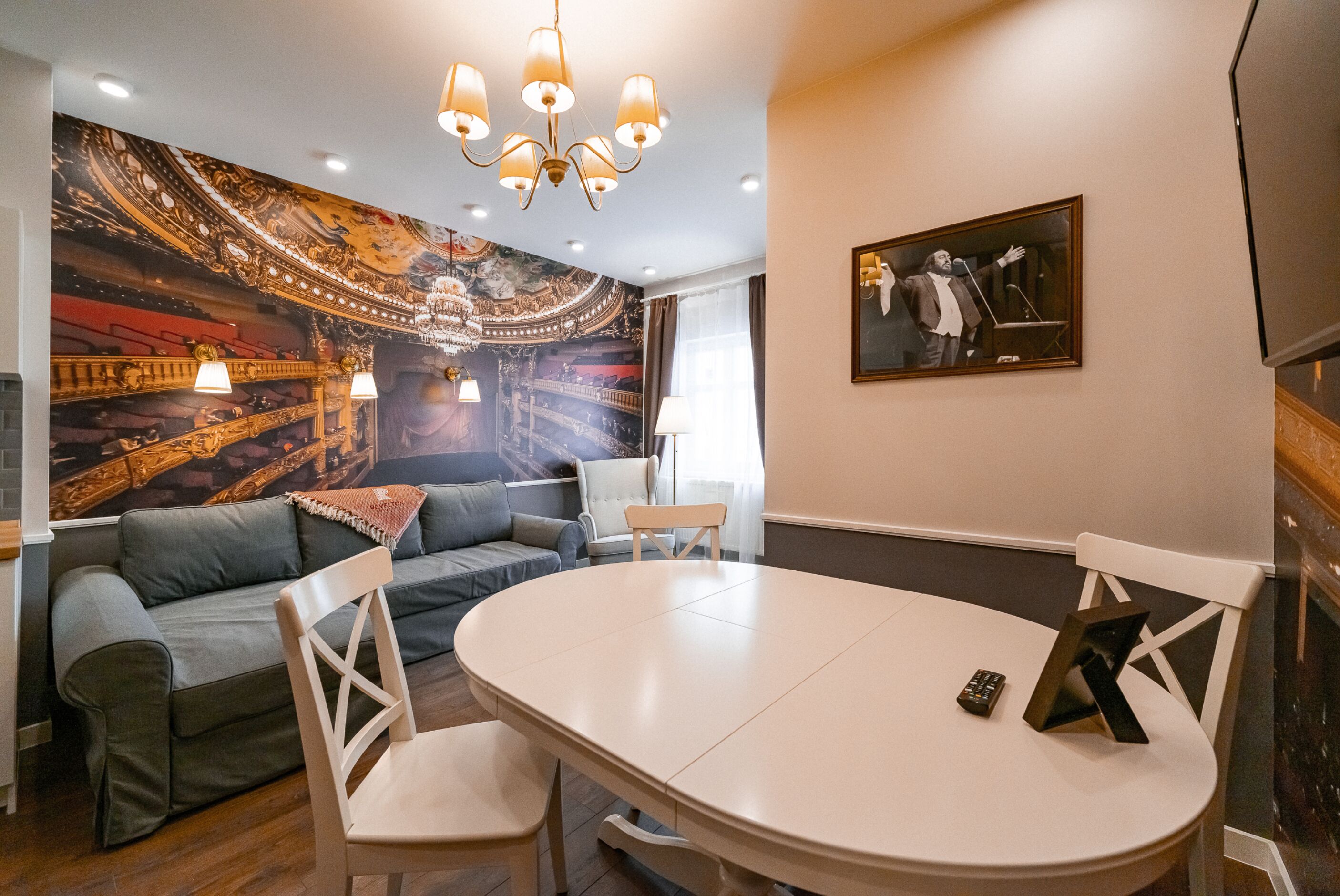 Un comedor con una mesa redonda, dos sillas, un sofá y un mural de un teatro en la pared.