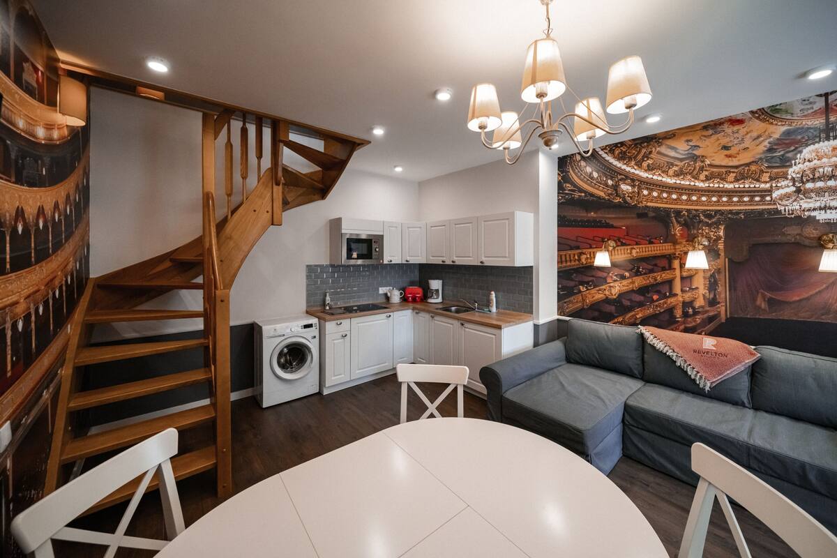 Cocina moderna con horno empotrado, microondas y fregadero. Una escalera de madera conduce a un nivel superior.
