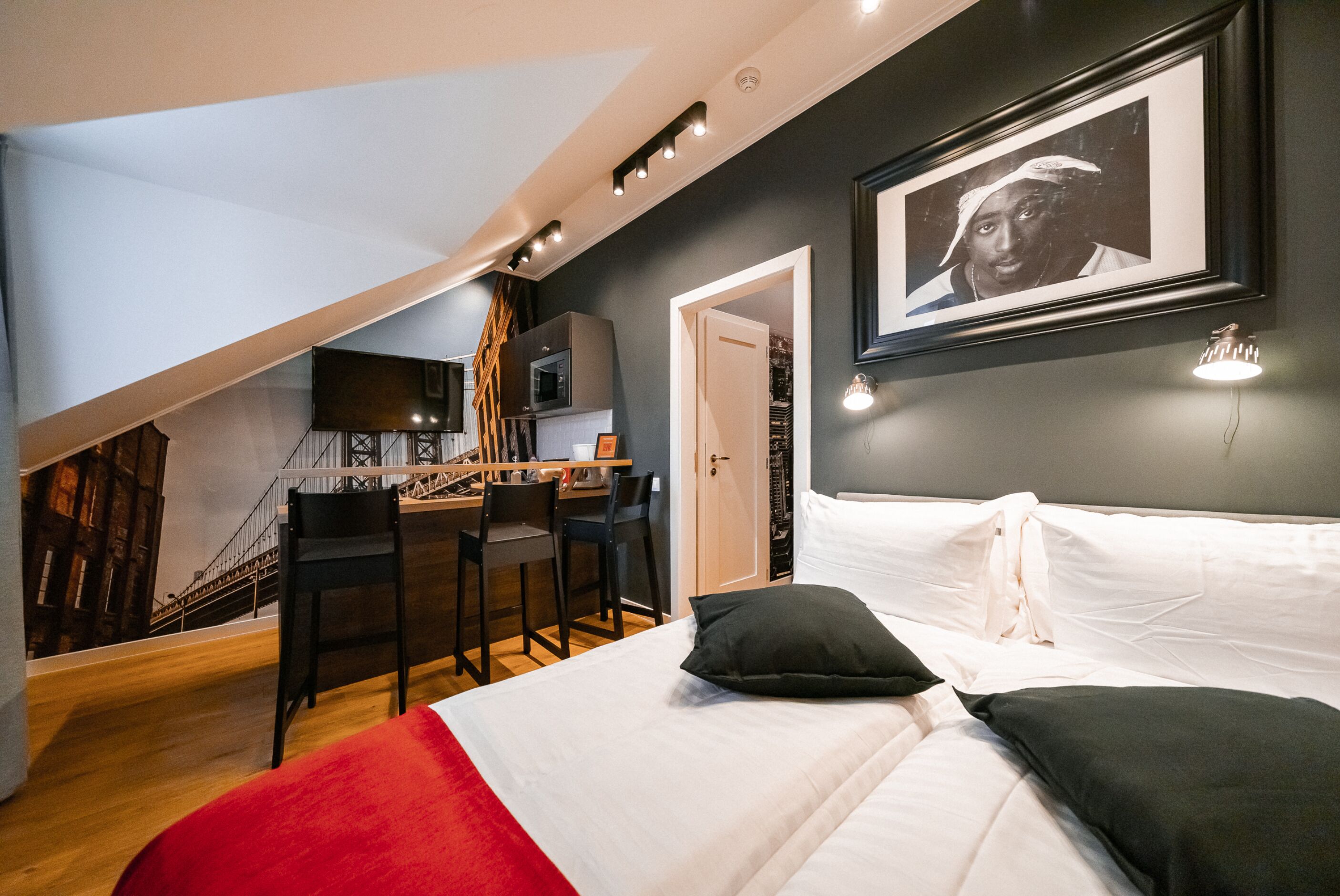 A bedroom with a bed, a desk, and a chair. There is a staircase leading to an upper level.