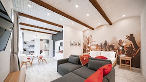 Una sala de estar moderna con un sofá gris, cojines rojos, una mesa de centro de madera y una zona de comedor con sillas blancas.