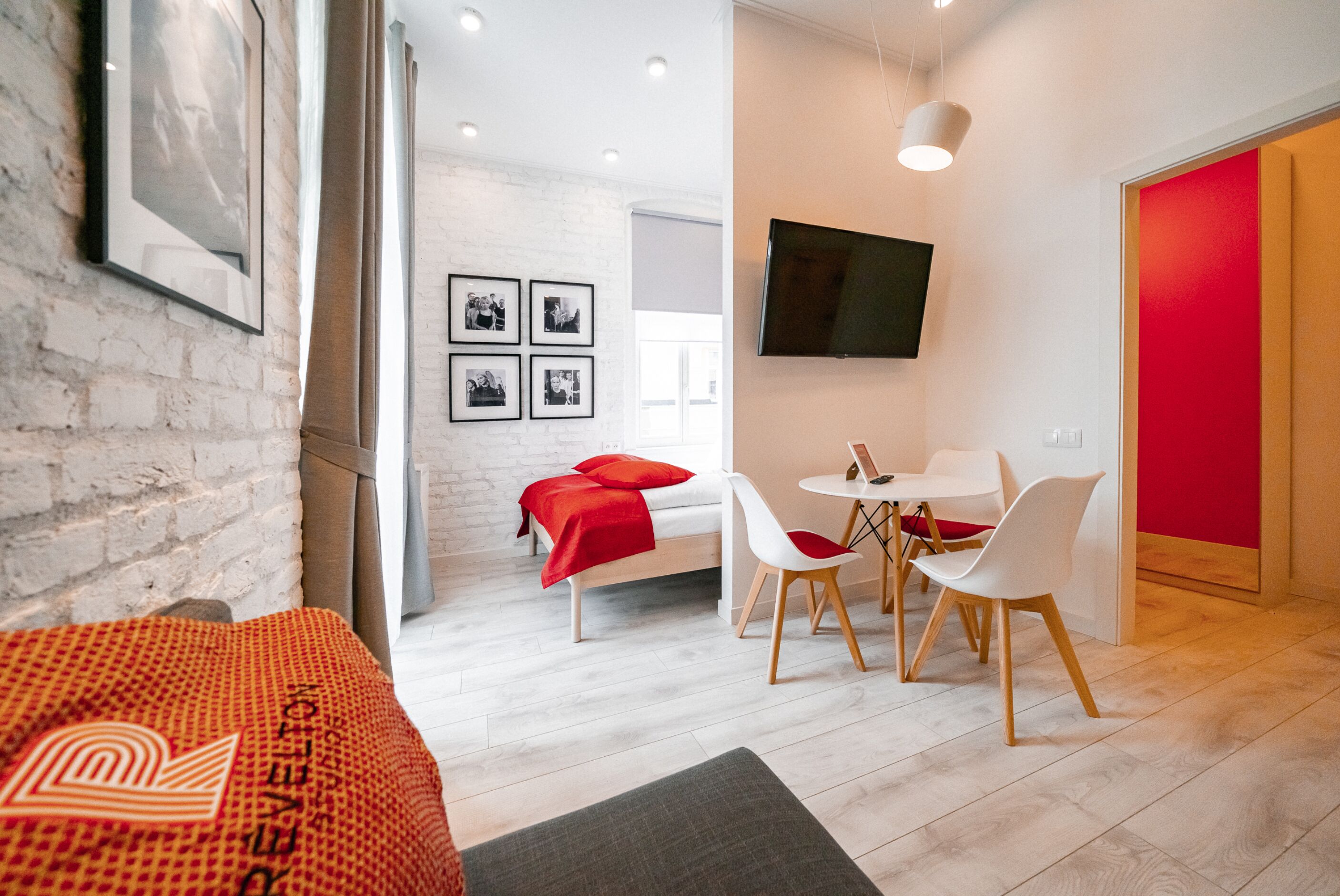 Una habitación de hotel moderna con una cama, una zona de comedor con sillas, un televisor montado en la pared y una pared de acento roja.