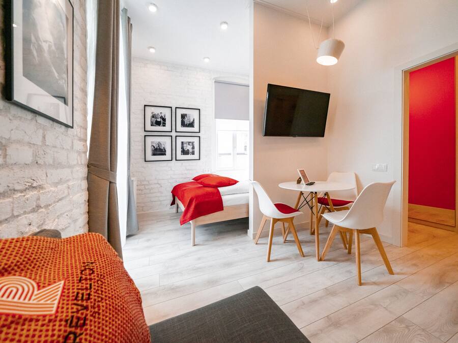 Una habitación de hotel moderna con una cama, una zona de comedor con sillas, un televisor montado en la pared y una pared de acento roja.