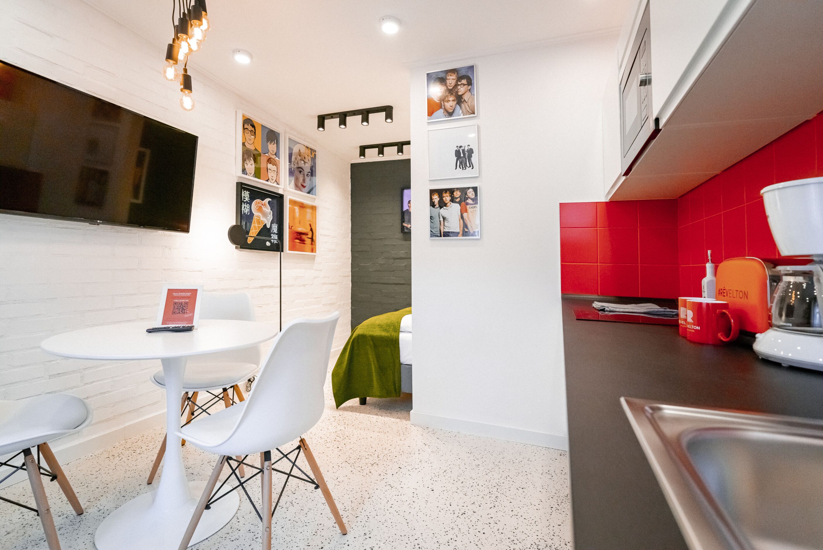 Una cucina moderna con piastrelle rosse, pareti bianche e zona pranzo con tavolo e sedie bianche.
