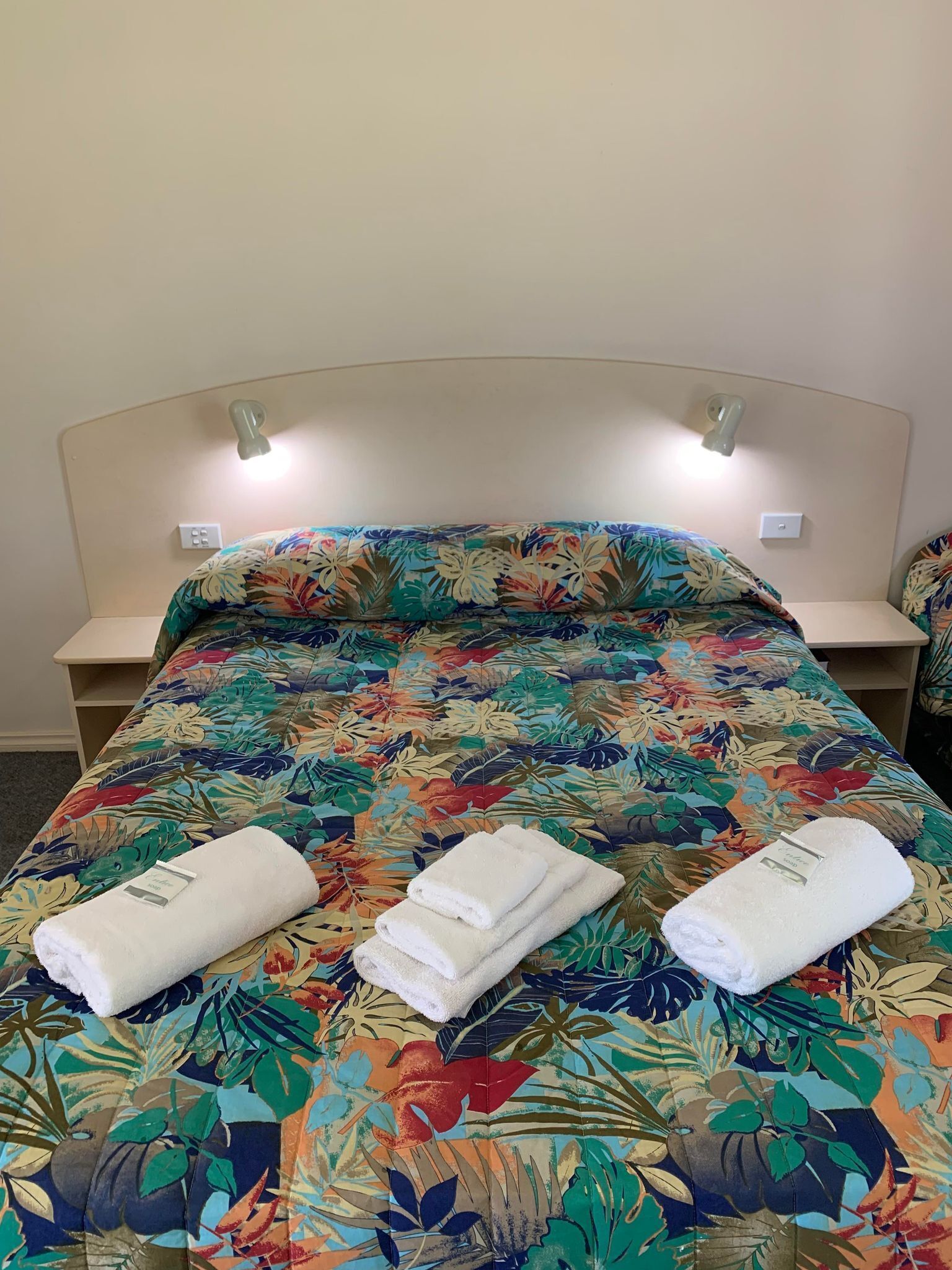 A bed with a floral bedspread, two bedside tables, and two wall-mounted lights.