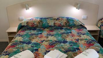 A bed with a floral bedspread, two bedside tables, and two wall-mounted lights.