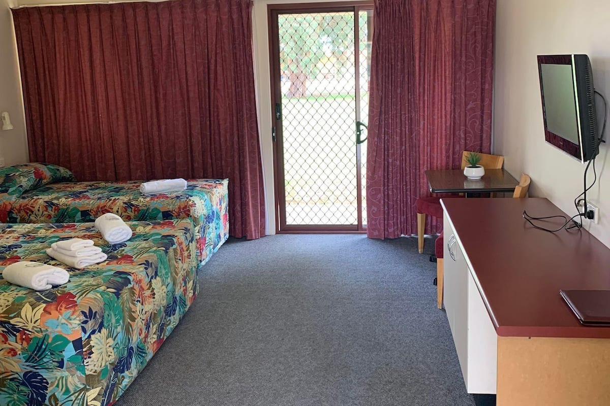 A hotel room with two beds, a desk, a television, and a sliding glass door to the outside.
