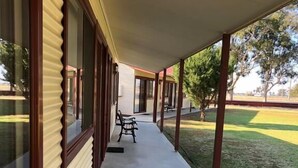 A covered walkway with a bench, leading to a building with large windows and a door. - Outback Quarters Motel Hay and Restaurant (Hay South)