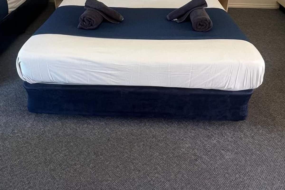 A hotel room with two beds, each with a headboard, white bedding, and dark blue pillows.