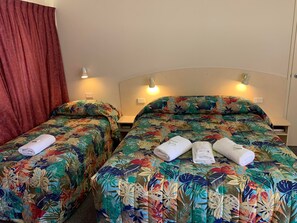 Dos camas individuales con ropa de cama floral, una cortina roja y lámparas de noche.