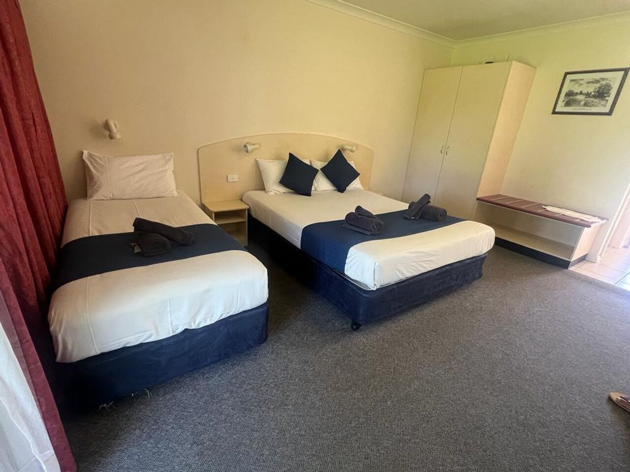 A hotel room with two beds, a small desk, and a wardrobe.