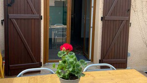 Una mesa de madera con una planta en maceta frente a un edificio con dos puertas de madera y un escaparate de vidrio.
