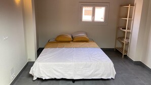 Un dormitorio con cama, dos almohadas, una ventana y un estante de madera.