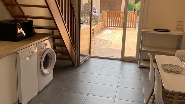 Cocina compacta con lavadora, zona de comedor con mesa y sillas, y una escalera que conduce a un patio exterior.