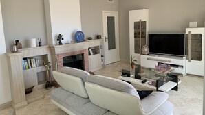 Een moderne woonkamer met een open haard, een bank, een televisie en een glazen salontafel.