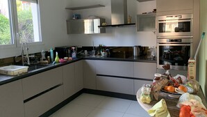 Een moderne keuken met een spoelbak, fornuis en oven. Er zijn kastjes, een raam en een aanrecht met diverse spullen.
