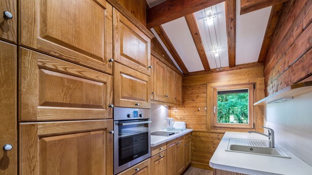 A compact kitchen with wooden cabinets, a built-in oven, and a window with a view of greenery. - Sunny 2-bedroom chalet in Megève, near slopes (Megève)