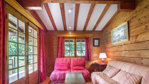 A cozy cabin room with a wooden interior, a sofa, a table, and large windows with curtains. - Sunny 2-bedroom chalet in Megève, near slopes (Megève)
