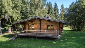 A wooden cabin with a porch, surrounded by a grassy area and trees. - Sunny 2-bedroom chalet in Megève, near slopes (Megève)