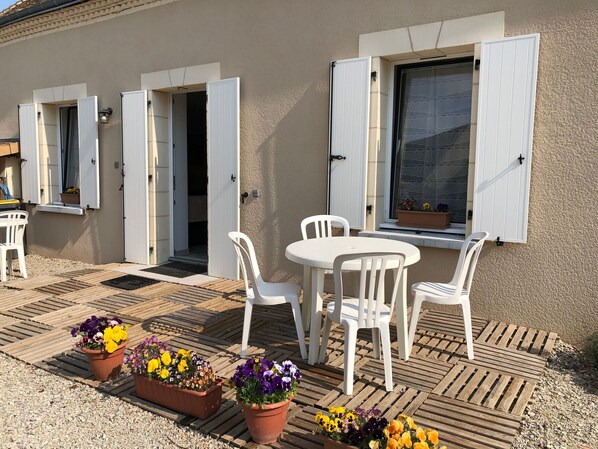 A patio with a round table and white chairs, surrounded by potted flowers. - Cottage by Orne River with garden and fishing, Pets allowed (Mézières-sur-Ponthouin)
