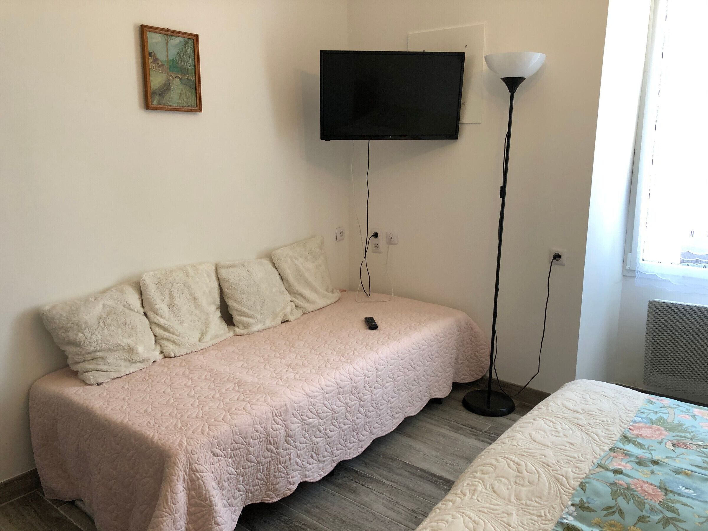 A bedroom with a bed, a television mounted on the wall, a floor lamp, and a window.